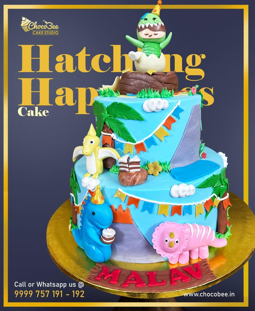 Two tier dinosaur cake with a hatching dino, dinosaur figurines and palm trees by Chocobee Cake Studio